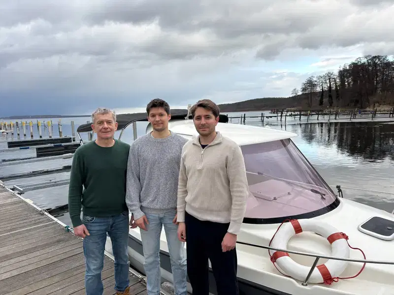 Andreas, Konstantin und Bastian Bothe stehen auf einem Steg vor einem Motorboot