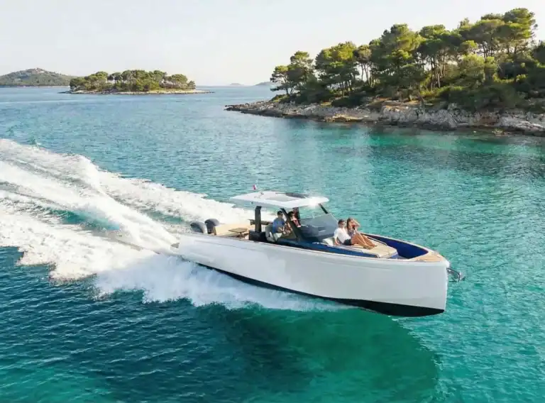 Modernes führerscheinpflichtiges Motorboot mit Passagieren bei einer Ausfahrt auf klarem, türkisfarbenem Wasser vor einer Insel.